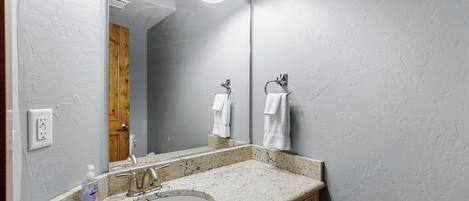 Ein Badezimmer mit Granittisch, Waschbecken, Spiegel und Holztür.