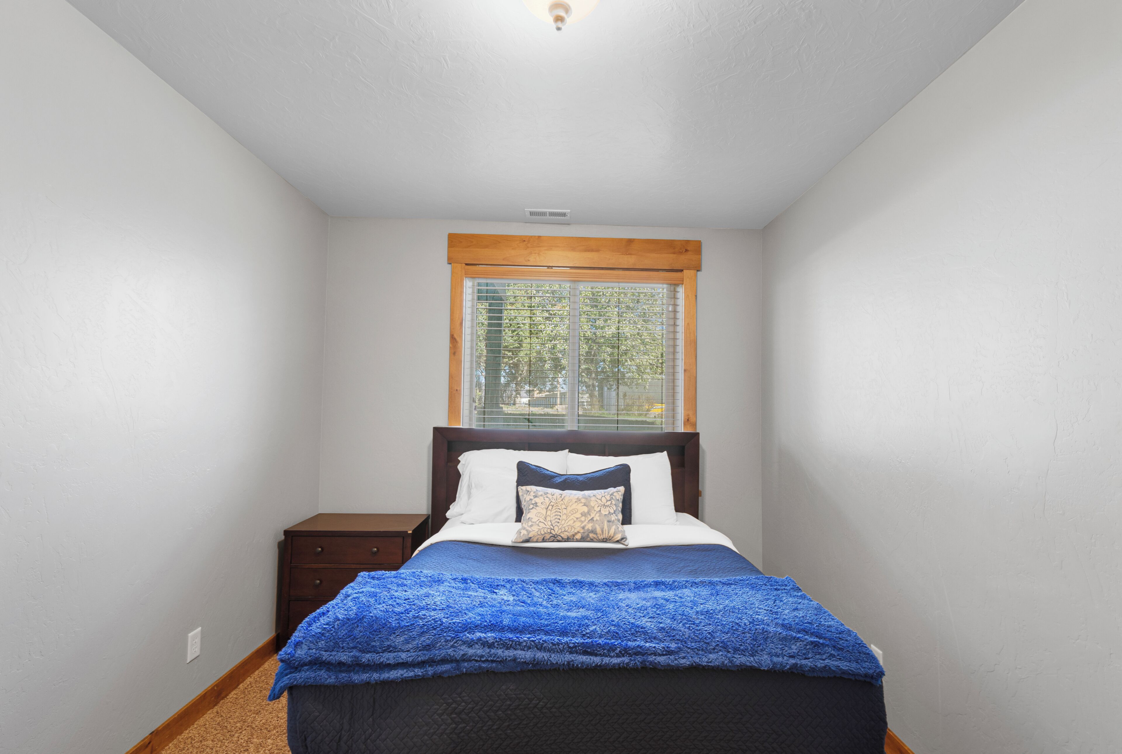 A bedroom with a bed, a window, a nightstand, and a wooden headboard.