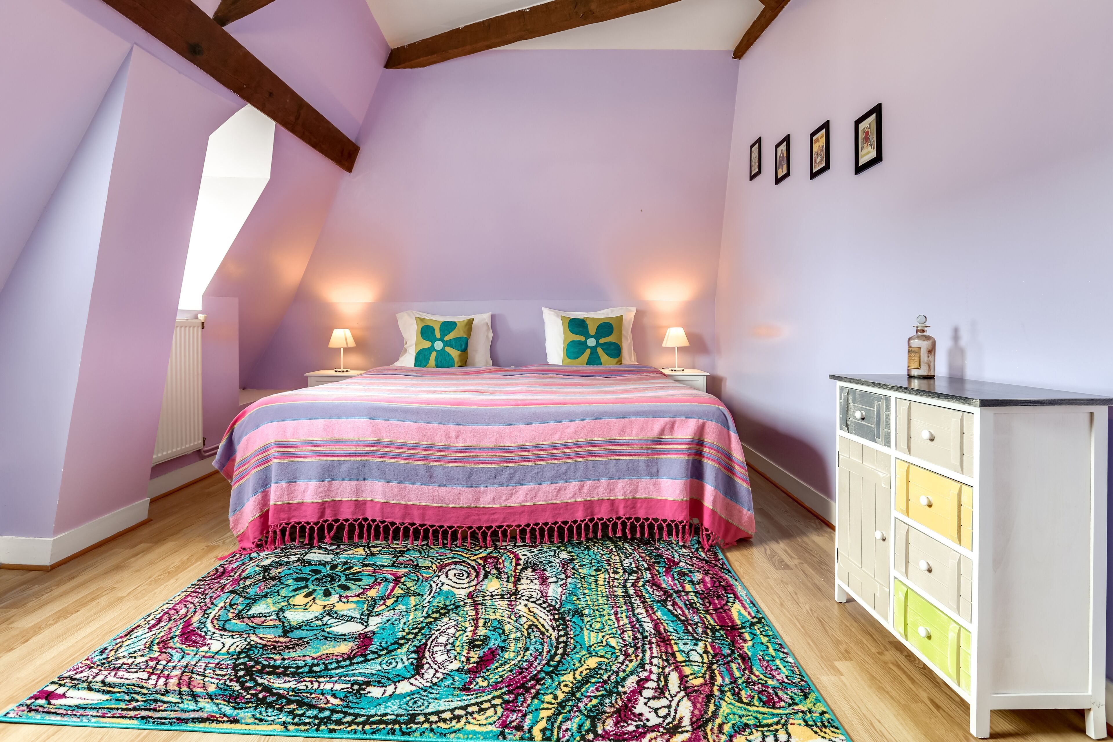 A bedroom with a bed, a colorful rug, a dresser, and a radiator.