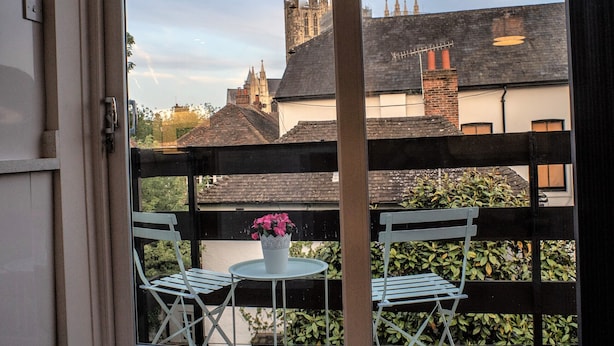 Un balcone con due sedie bianche e un tavolino con un vaso di fiori.