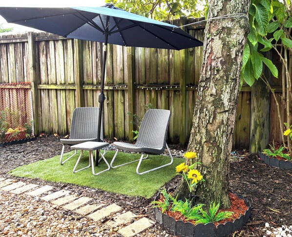 Un patio con dos sillones de mimbre, una sombrilla azul y un árbol.