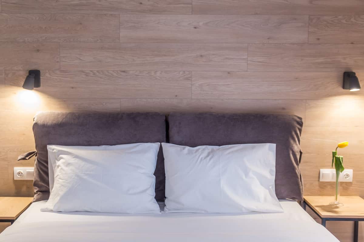A neatly made bed with white sheets and pillows, a wooden headboard, and two bedside tables with lamps.