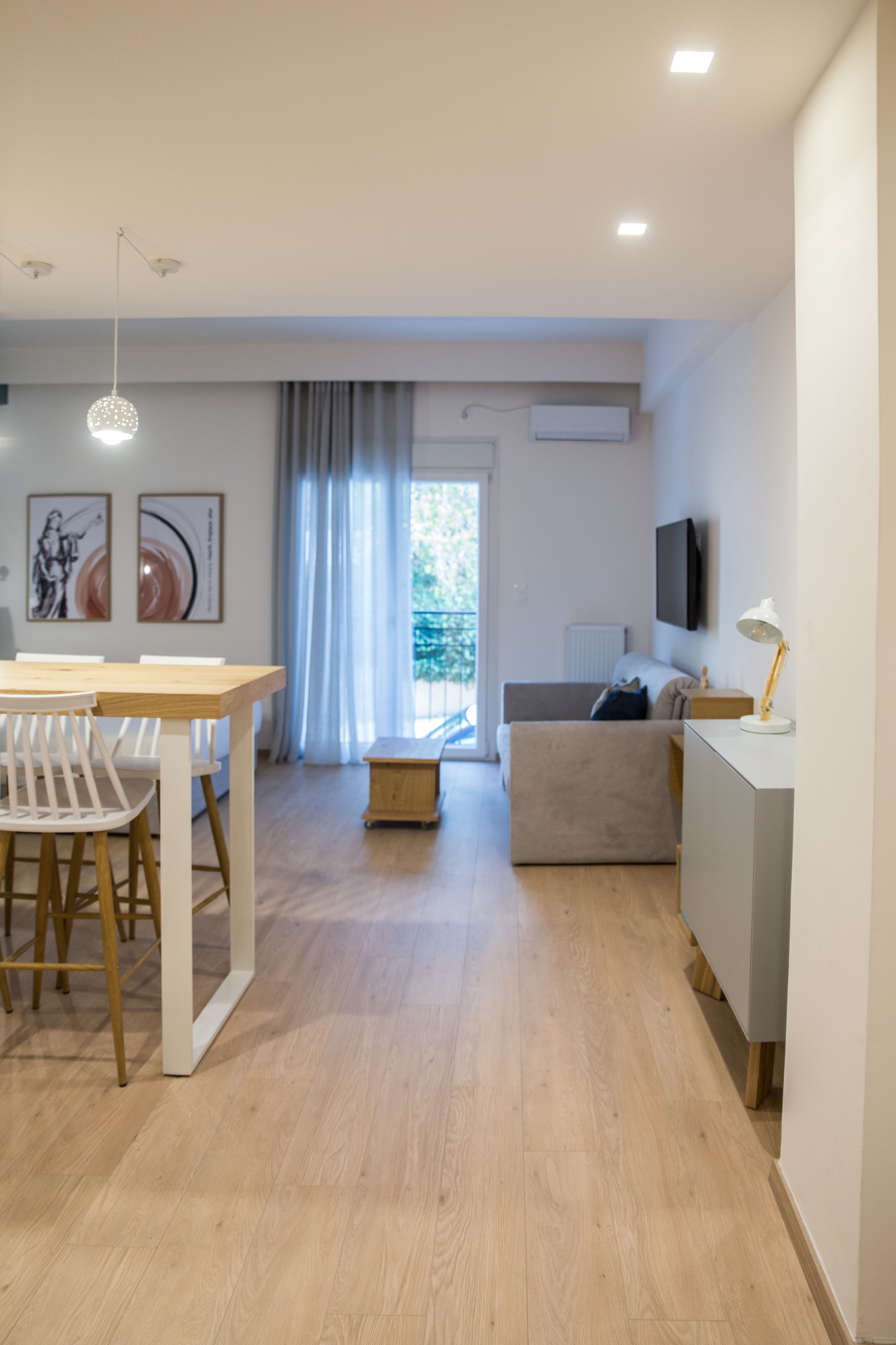 A modern living room with a dining area, a sofa, and a TV mounted on the wall.