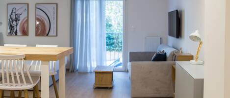 A modern living room with a dining area, a sofa, and a TV mounted on the wall.