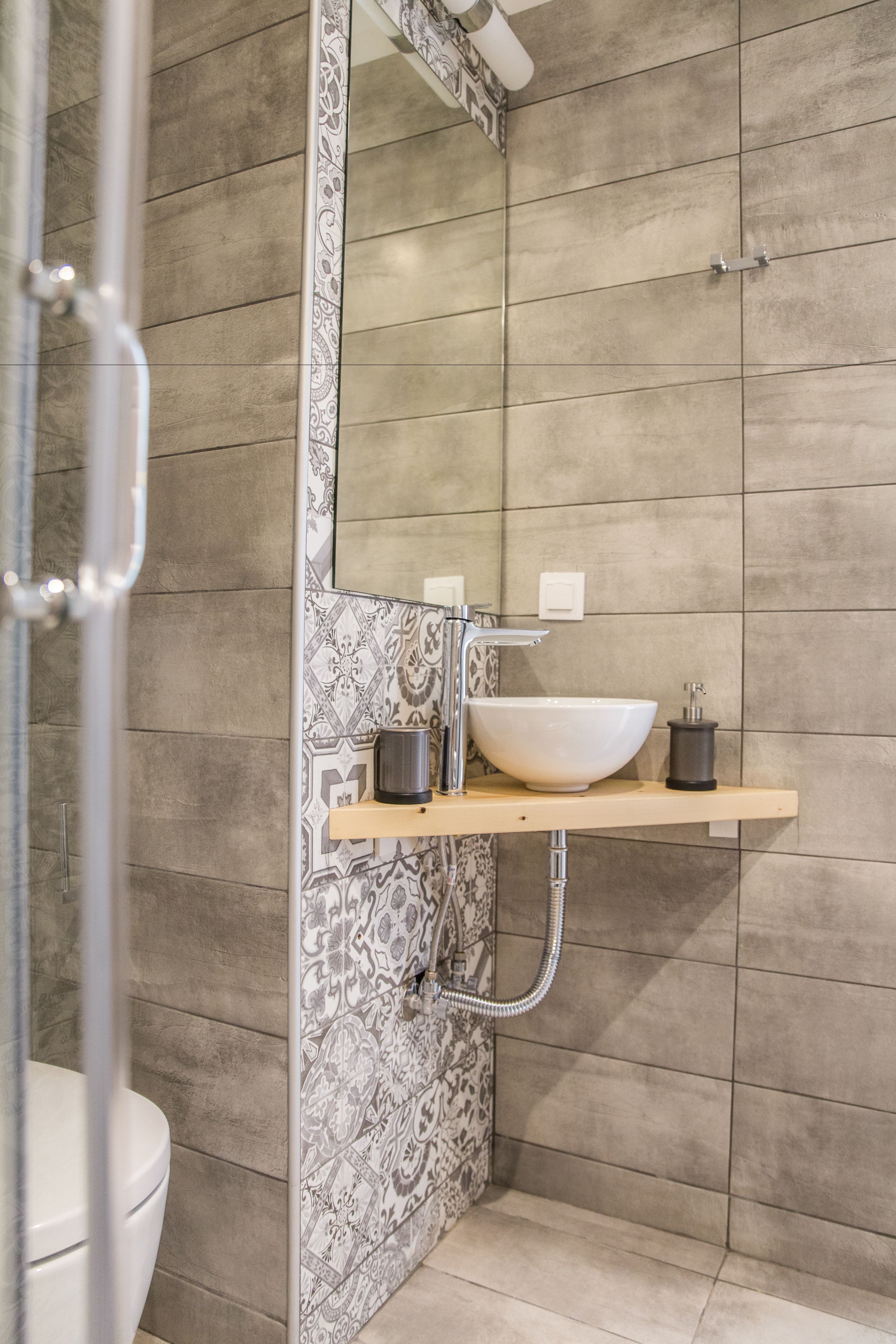 Un baño con un espejo grande, un lavabo independiente y baldosas estampadas.