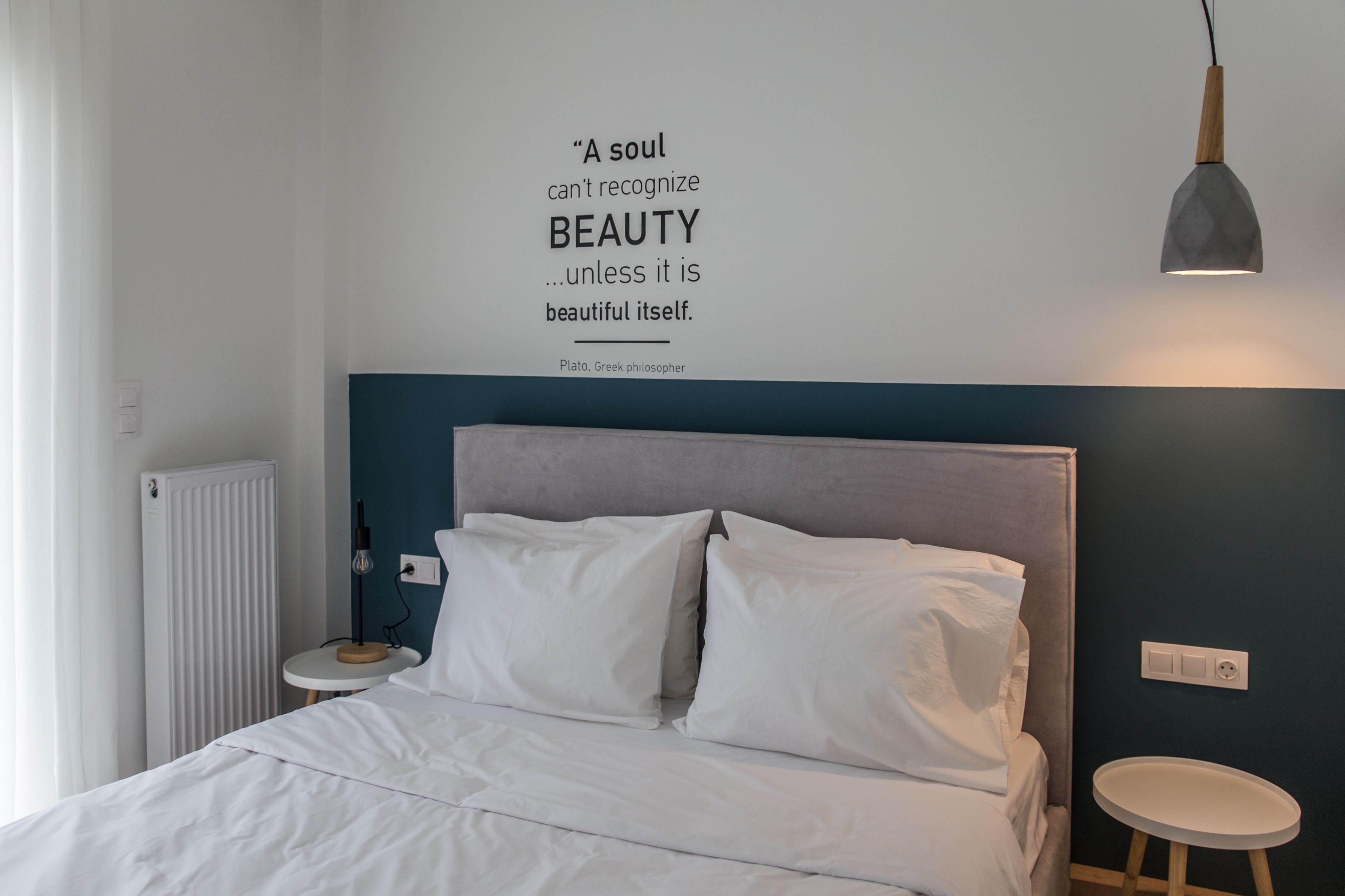 A bedroom with a bed, a bedside table, a wall-mounted light, and a quote about beauty.