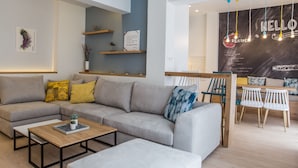 Una sala de estar moderna con un sofá seccional gris, una mesa de centro de madera y un comedor con sillas blancas y una mesa de madera.