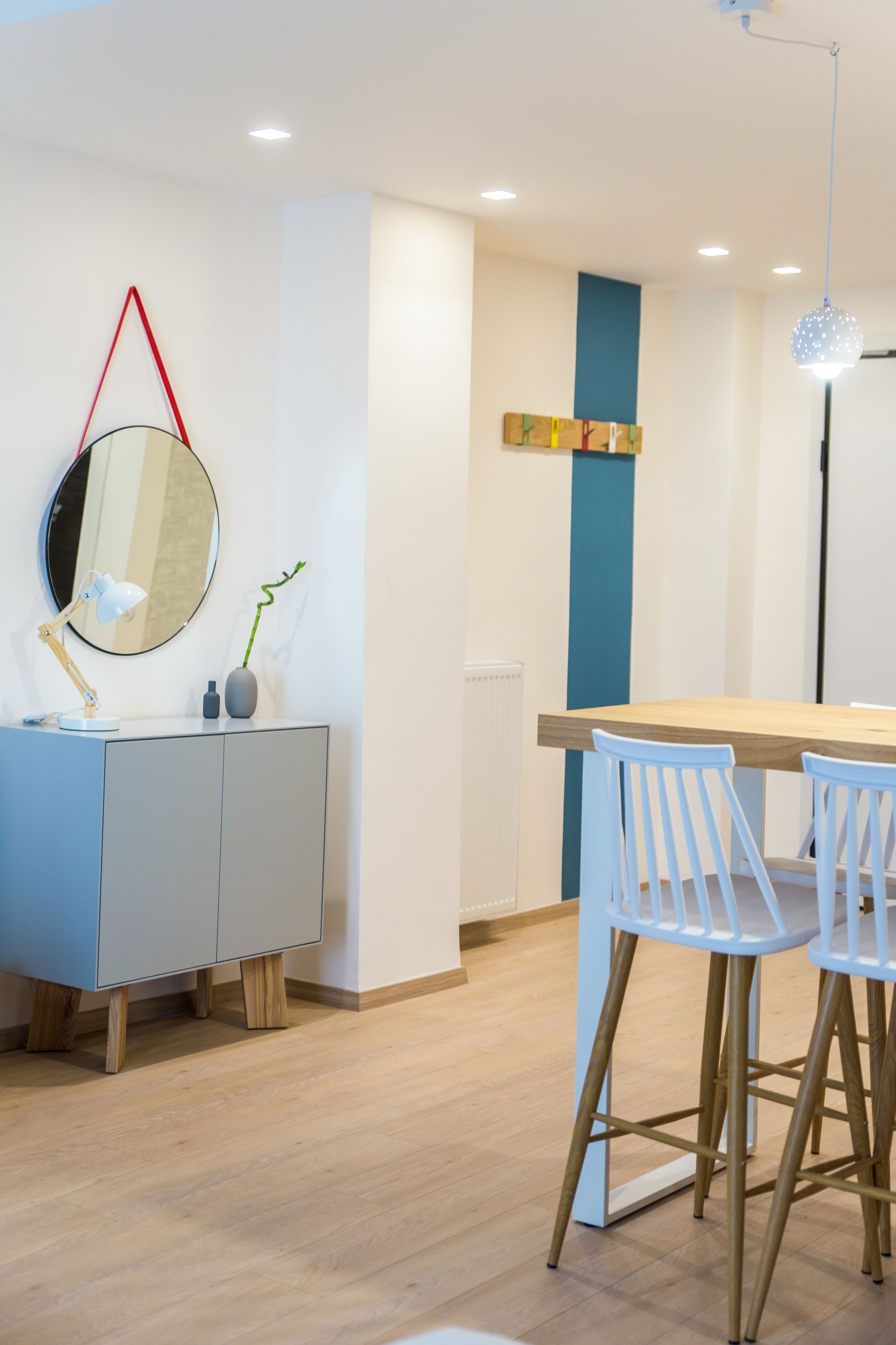 Eine moderne Küche mit einem Holztisch, weißen Stühlen, einem runden Spiegel und einer blauen Wand.