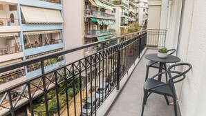 Un balcón con una pequeña mesa y sillas, con vistas a un patio donde se ven coches aparcados y edificios cercanos.