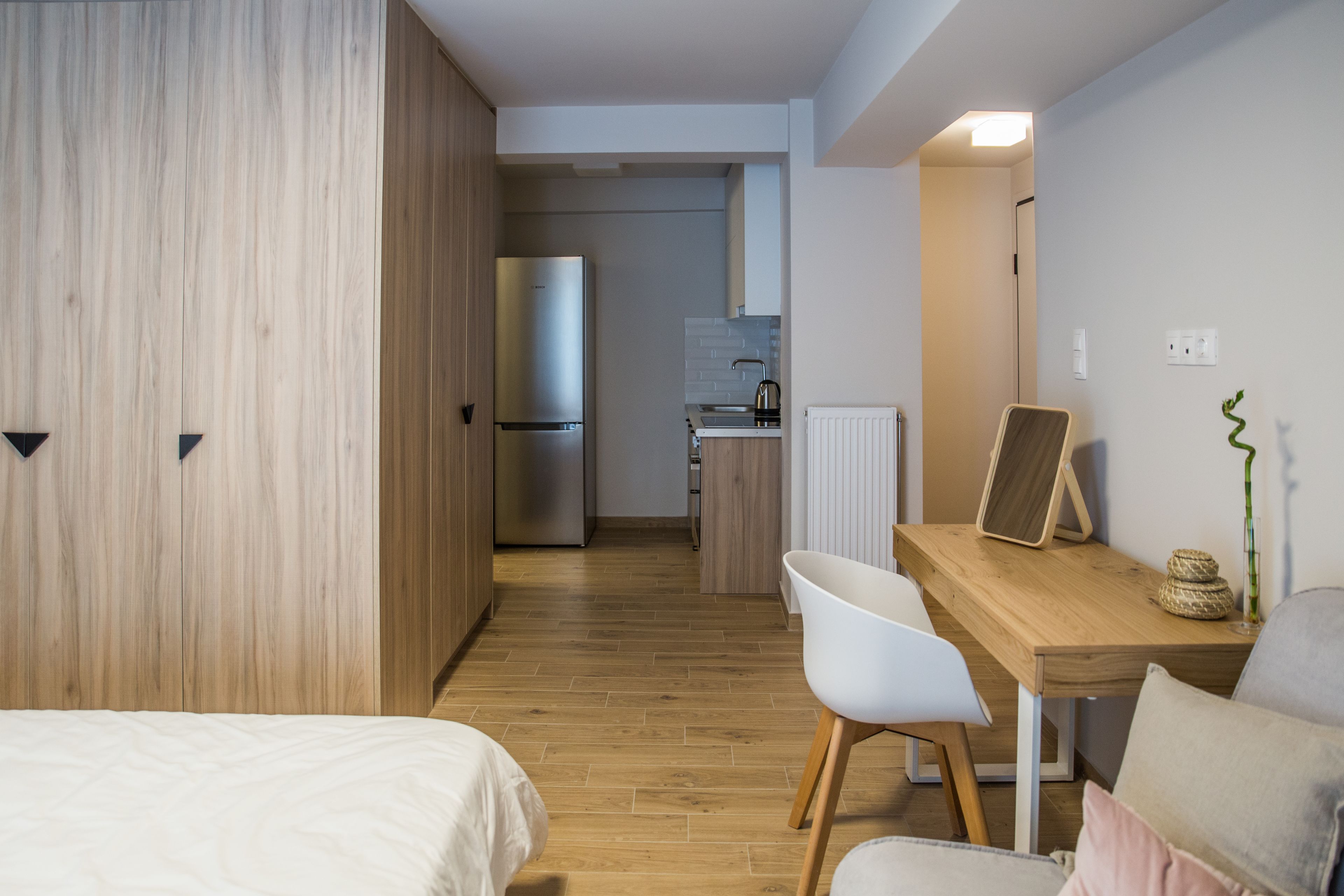 Een moderne hotelkamer met een houten kledingkast, een bed, een bureau met stoel, een kitchenette en een radiator.