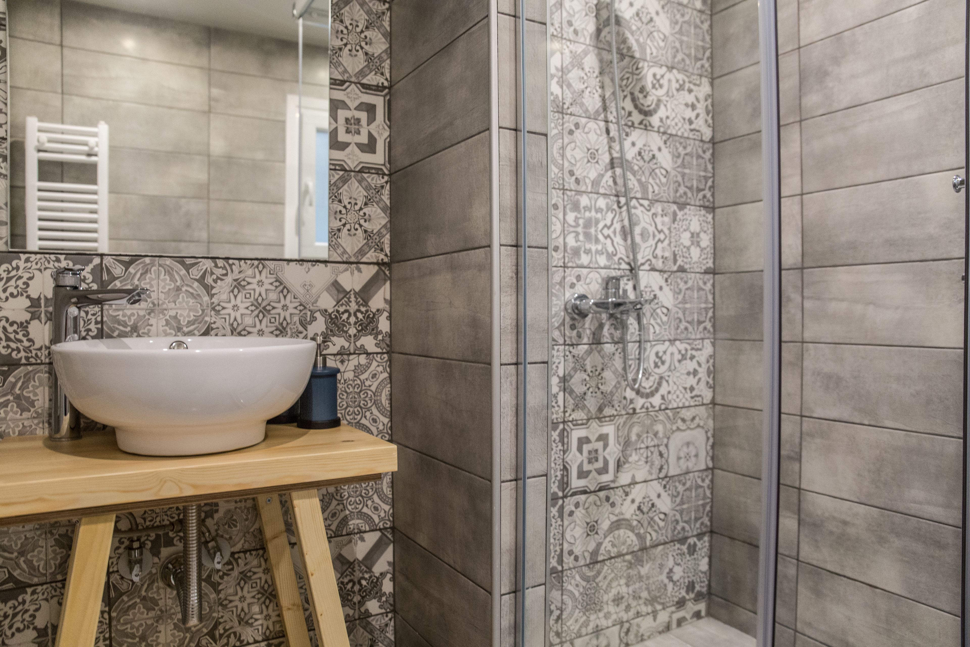 Un baño con un lavamanos grande, un espejo y una zona de ducha con azulejos estampados.