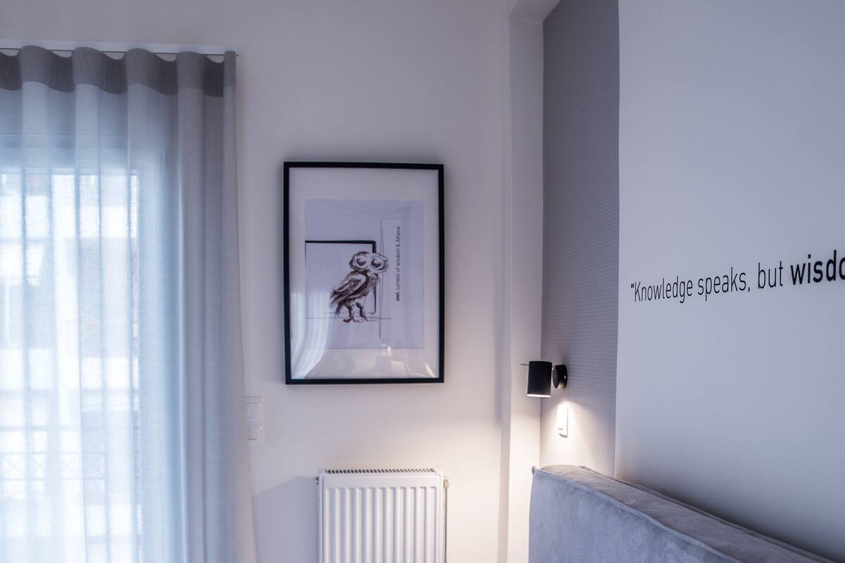 A modern bedroom with a neatly made bed, a framed artwork above it, and a motivational quote on the wall.