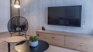 Una sala de estar moderna con una mesa redonda, una silla negra, una planta en maceta, un aparador de madera y un televisor montado en la pared.