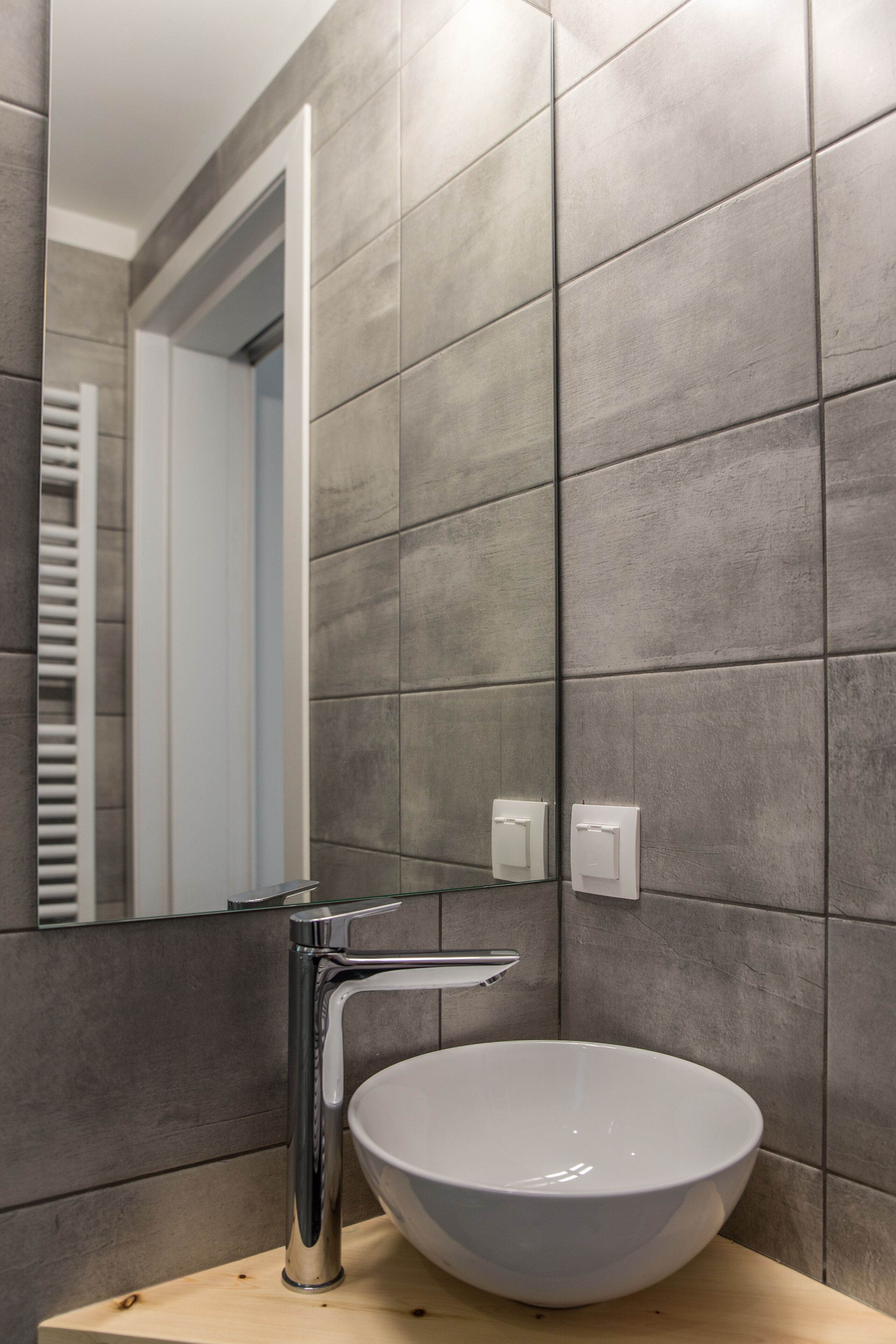 Une salle de bain moderne avec un grand lavabo blanc, un robinet chromé et un miroir qui reflète une porte et un porte-serviettes.