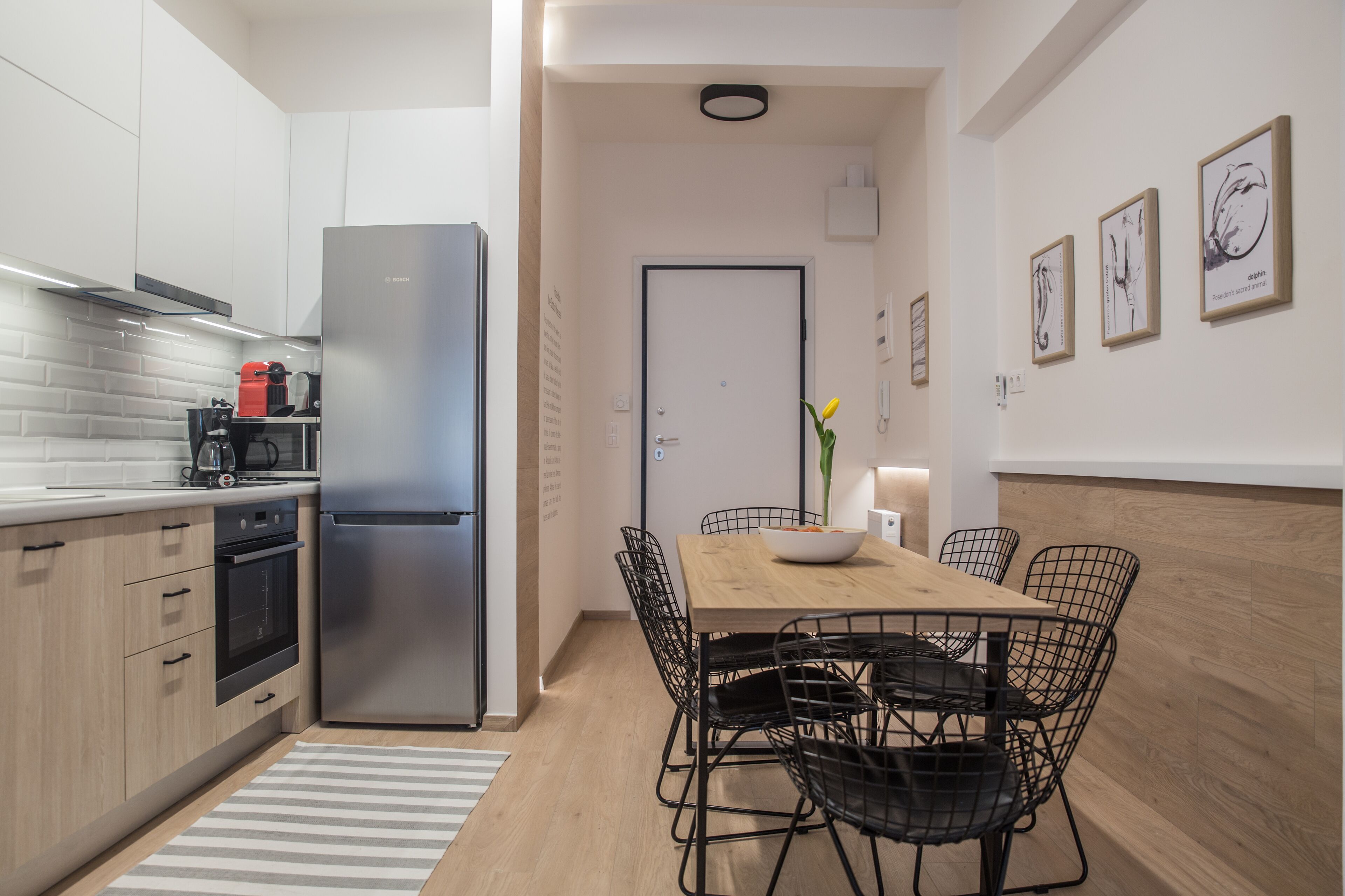 Una cucina moderna con frigorifero in acciaio inox, mobili in legno e zona pranzo con tavolo in legno e sedie in fil di ferro.