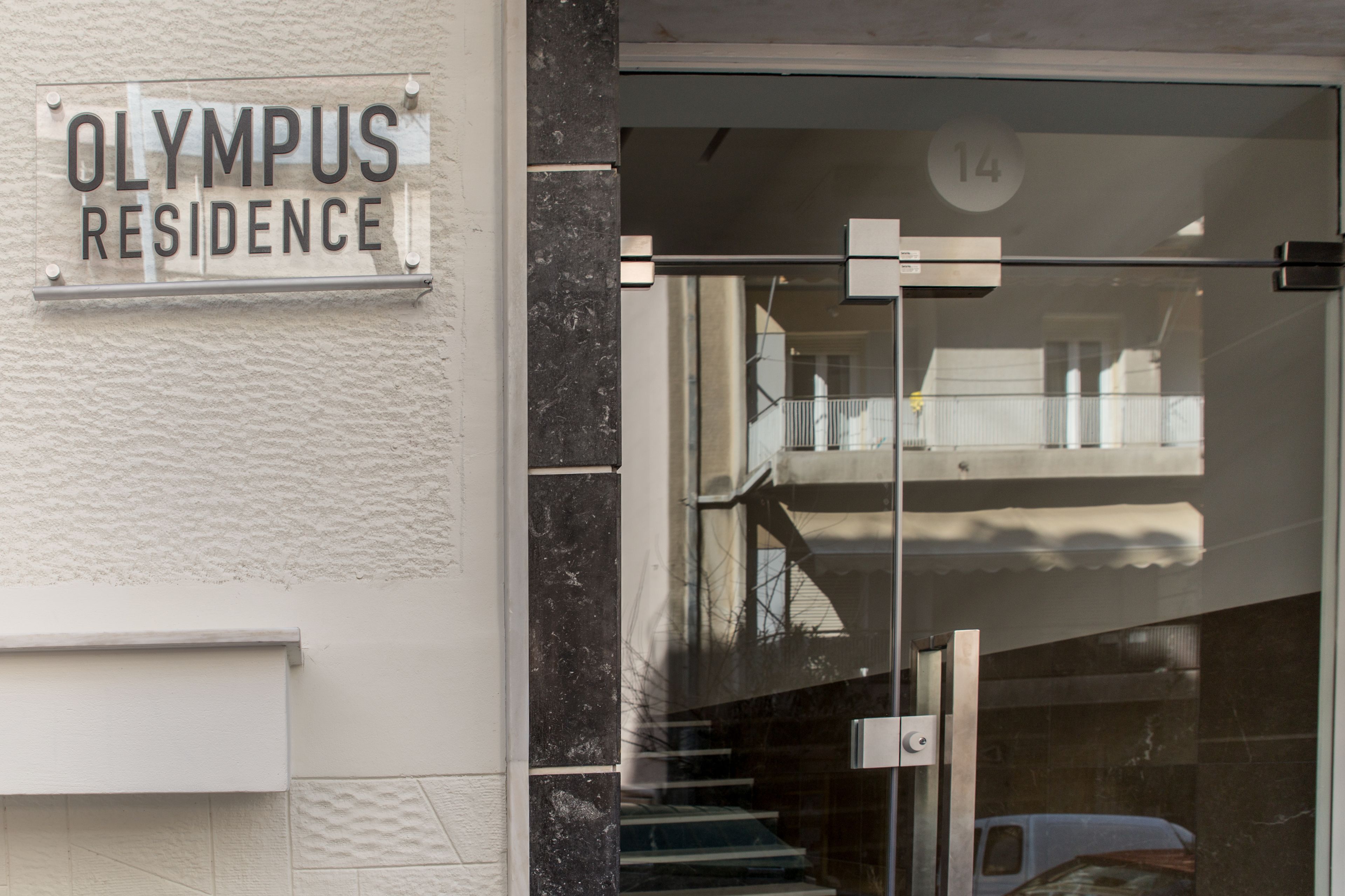 Entrada de un edificio con un letrero que dice "OLYMPUS RESIDENCE" y el número "14" en la puerta.