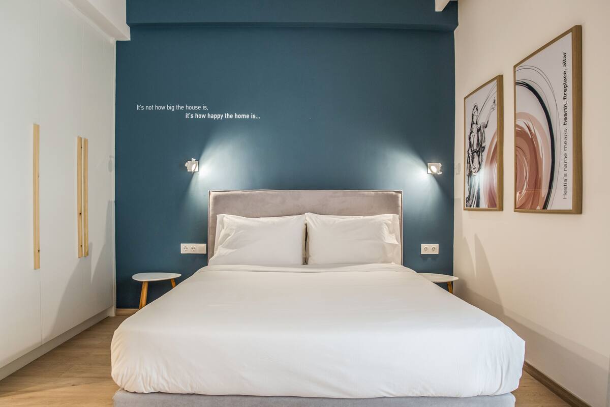 A bedroom with a large bed, two bedside tables, a blue accent wall, and a quote on the wall.