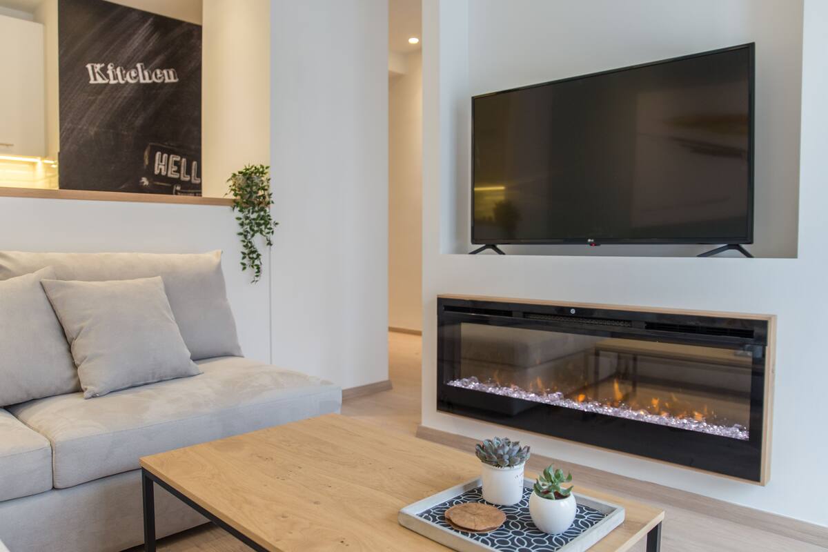 A modern living room with a sofa, a coffee table, a flat-screen TV, and a fireplace.