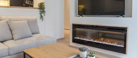 A modern living room with a sofa, a coffee table, a flat-screen TV, and a fireplace.