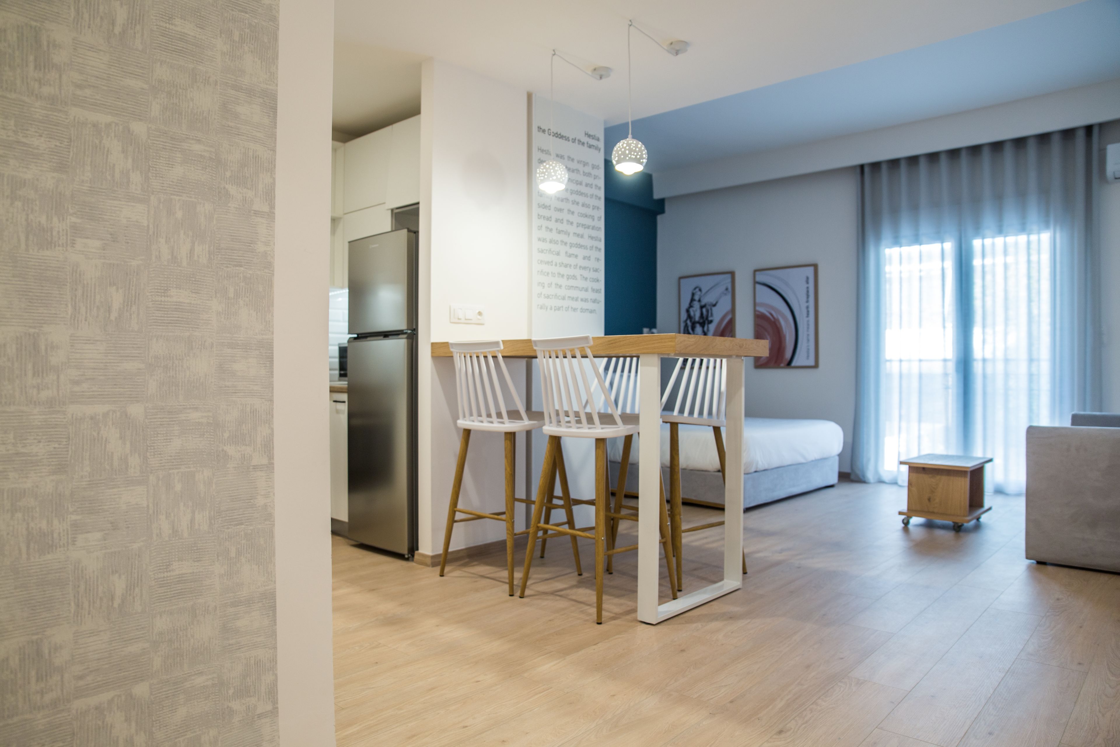 Una cocina moderna con refrigerador, un comedor con dos sillas blancas, una mesa de madera y un carrito pequeño.