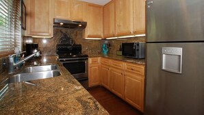 Una cocina con encimeras de granito, electrodomésticos de acero inoxidable, armarios de madera y un microondas empotrado.