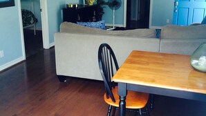 Una sala de estar con un sofá, una mesa de comedor con sillas, un televisor montado en la pared y una puerta azul con un letrero que dice 'WELCOME'.