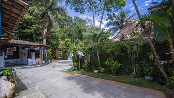 A paved pathway leading to a building with a tiled roof, surrounded by lush greenery and palm trees.