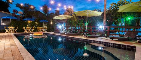 A swimming pool with tiled edges, lounge chairs, and umbrellas.