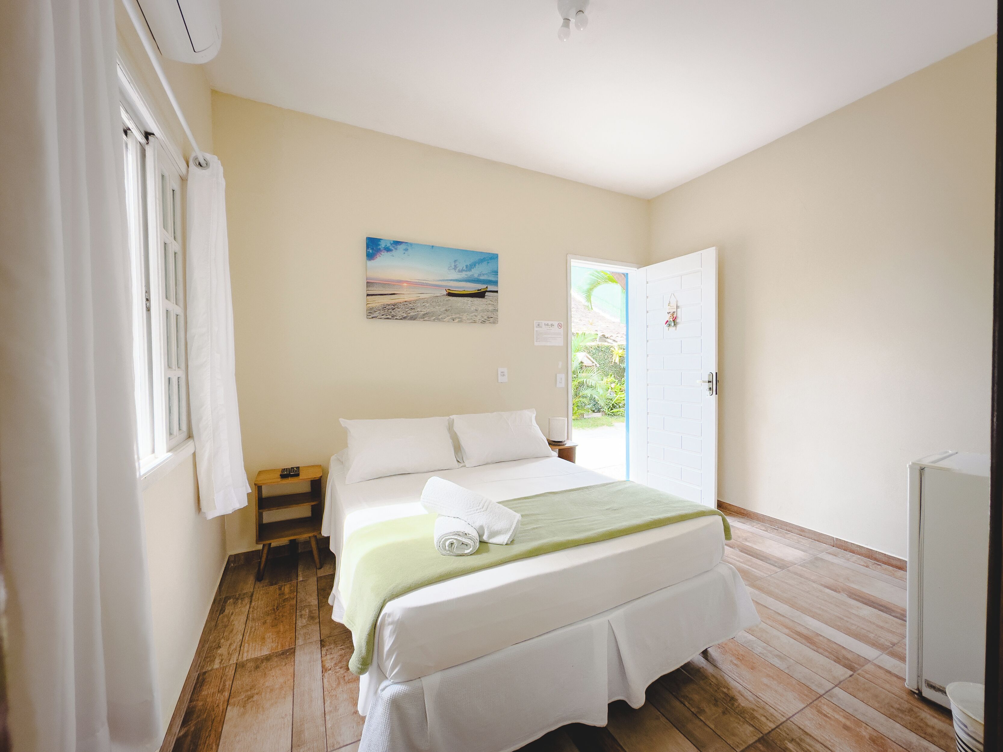 A bedroom with a bed, a nightstand, a painting, and a door leading to a balcony.