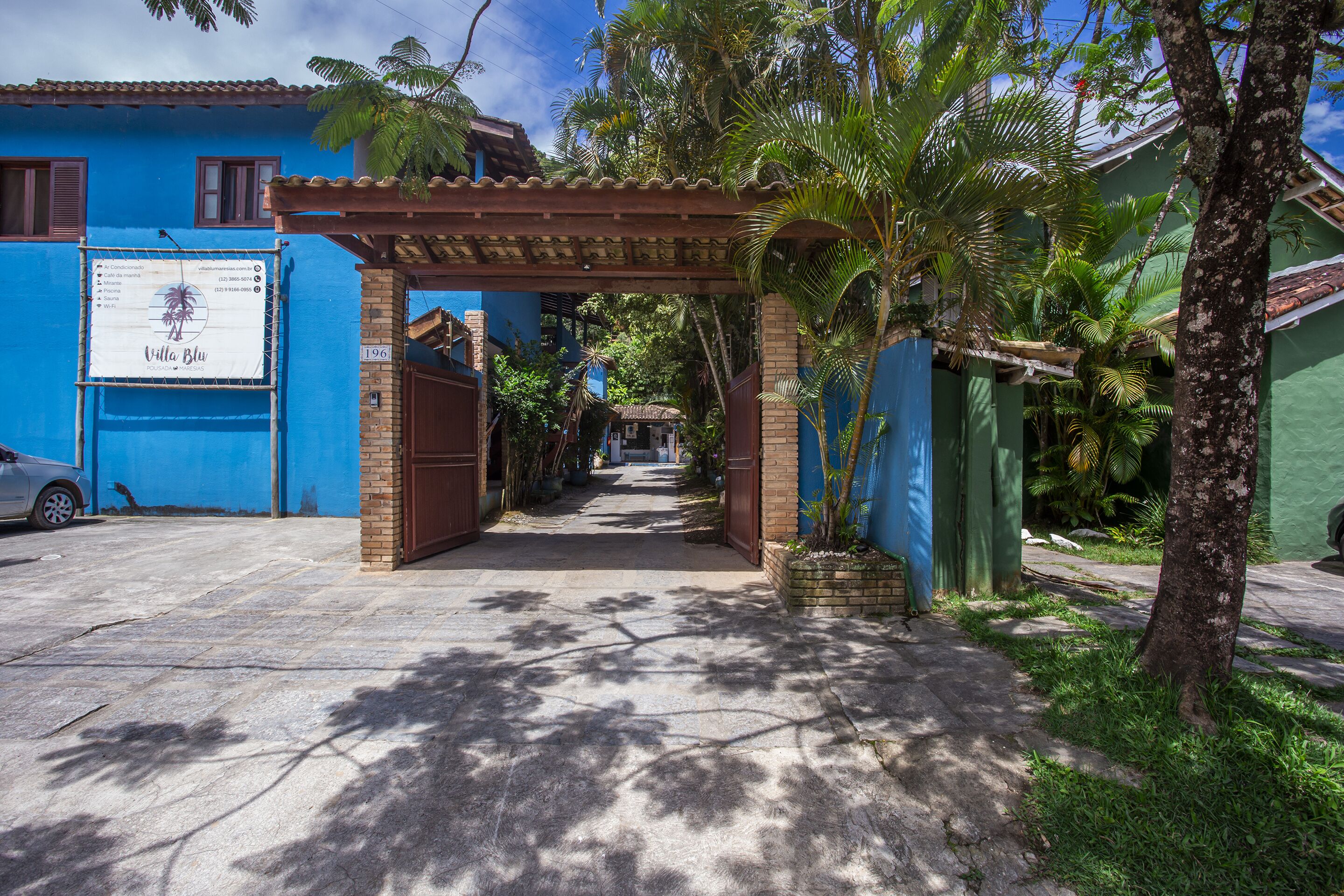 Un camino que lleva a un edificio de fachada azul, una pérgola y un cartel.