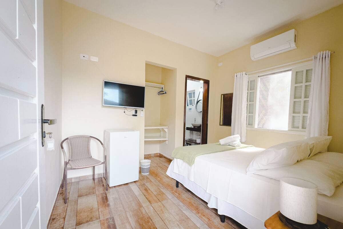 Habitación de hotel con cama, escritorio, silla, televisor y baño visible a través de una puerta abierta.