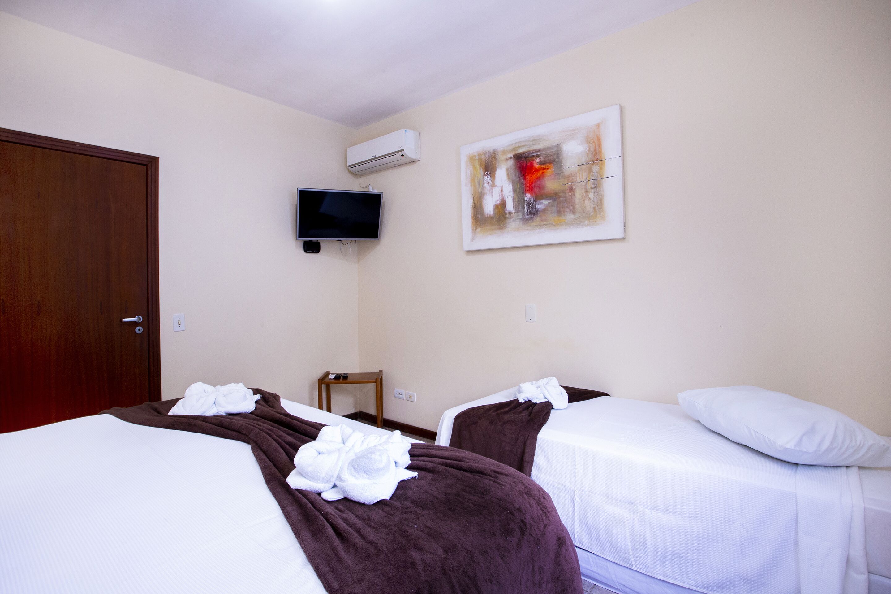 A hotel room with two beds, a TV, an air conditioner, and a painting on the wall.