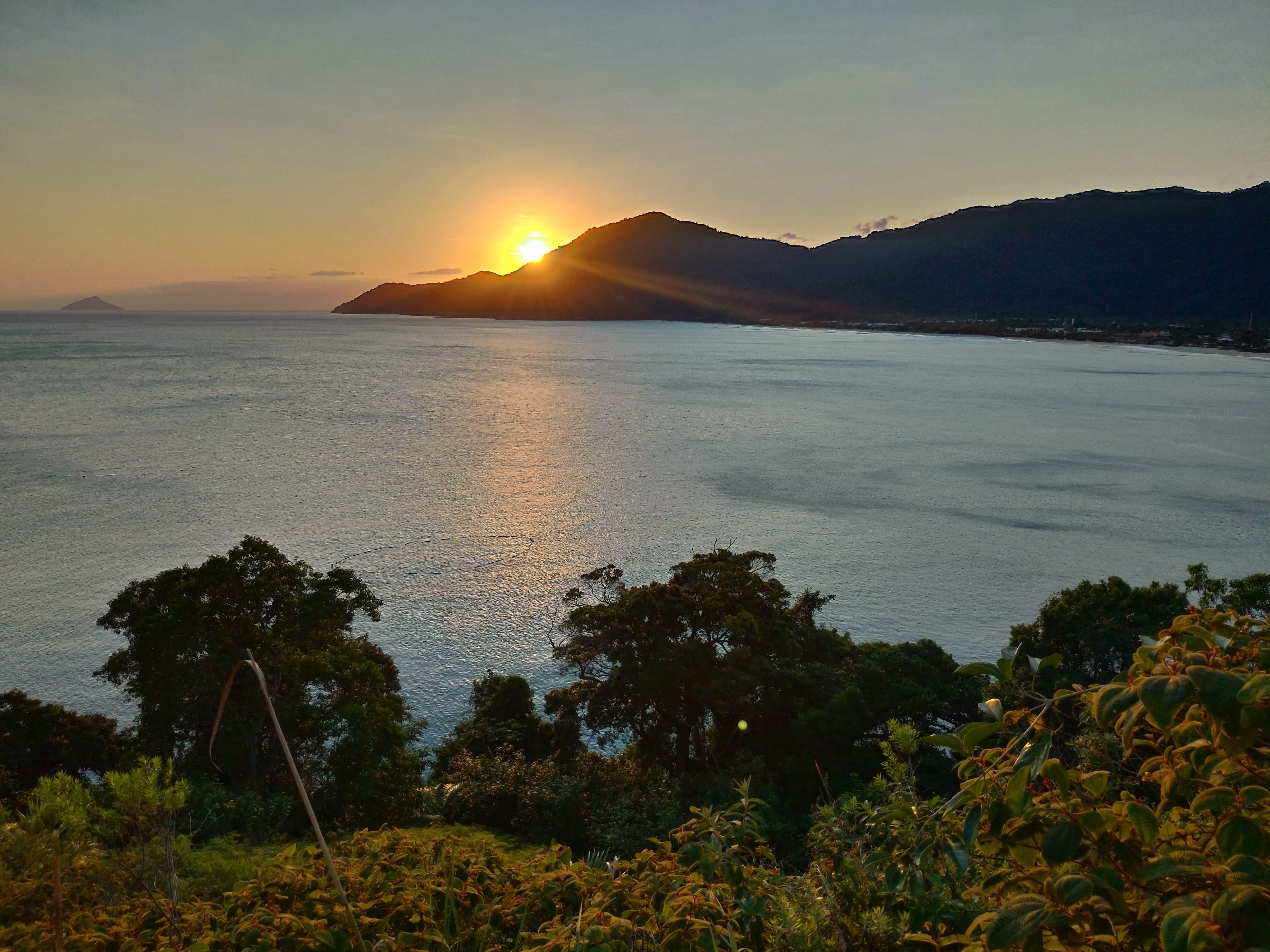 A sunset over a calm sea with a mountain in the background.