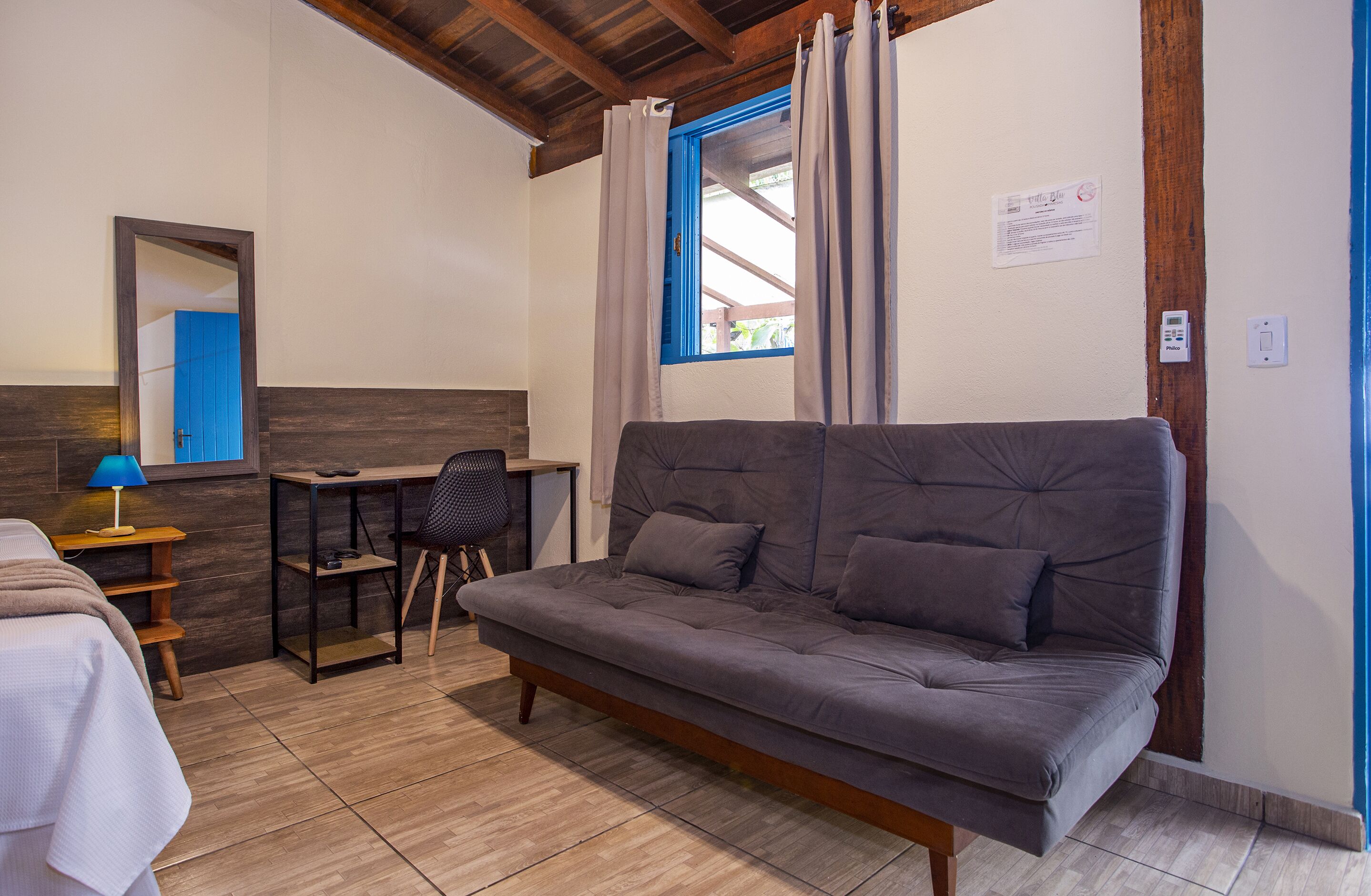 Ein Zimmer mit grauem Sofa, einem Holztisch, einem Stuhl und einem Bett.