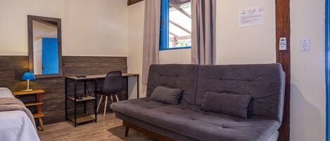 Ein Zimmer mit grauem Sofa, einem Holztisch, einem Stuhl und einem Bett.