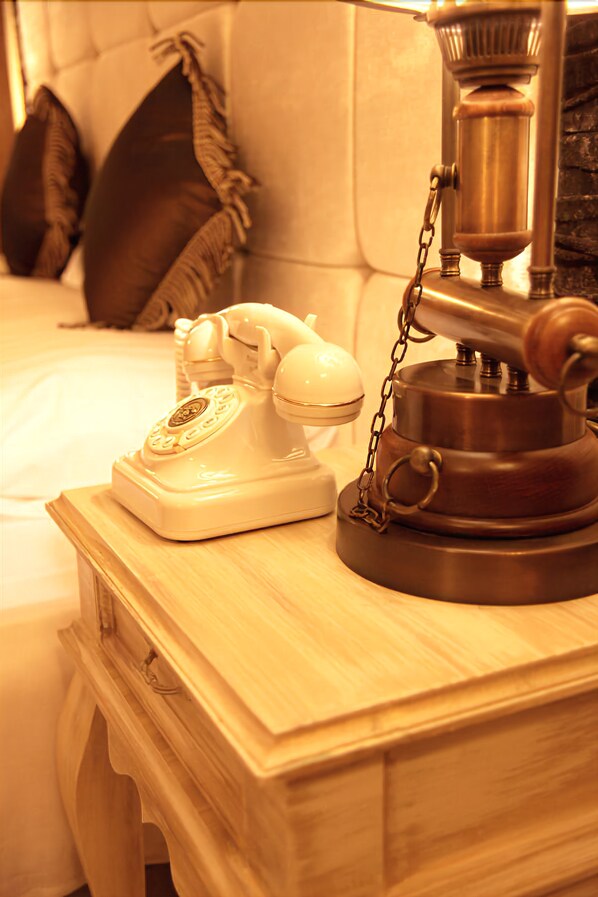 A vintage rotary phone and a brass coffee pot on a wooden nightstand in a hotel room.