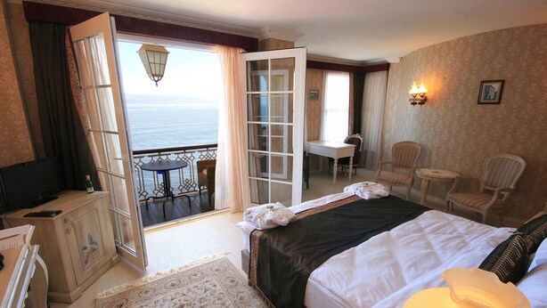 A hotel room with a bed, a desk, a chair, a television, and a view of the sea. - Trilyali Butik Otel (Mudanya)