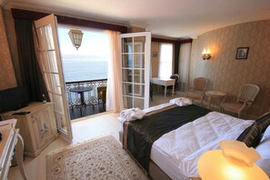 A hotel room with a bed, a desk, a chair, a television, and a view of the sea.