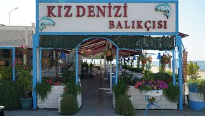 A seaside restaurant named KIZ DENİZİ BALIKÇİSİ with outdoor seating and hanging flower baskets. - Trilyali Butik Otel (Mudanya)