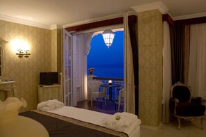 Habitación de hotel con cama, televisión, una mesita con sillas y balcón con vista al mar.