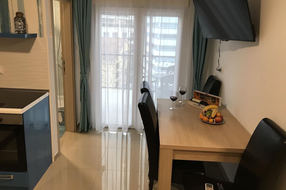 Ein moderner Essbereich mit einem Holztisch, zwei Stühlen, einem an der Wand montierten Fernseher und einem Fenster mit durchsichtigen Vorhängen.