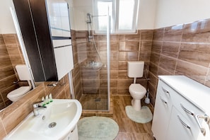 A modern bathroom with a glass-enclosed shower, a white sink, and two toilets. - Apartmani Belani (Herceg Novi)