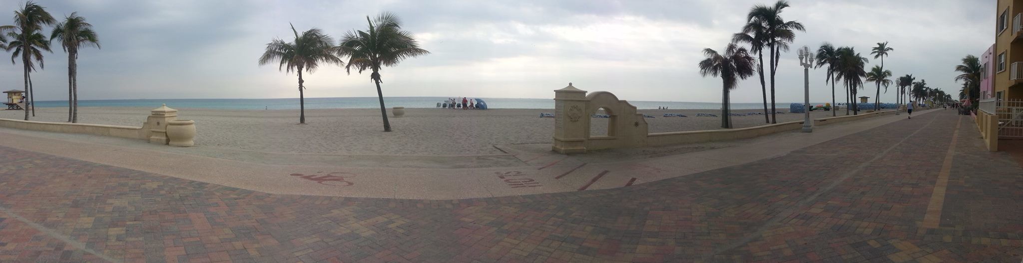 Eine Uferpromenade mit Palmen, ein Strand im Hintergrund und ein Gebäude auf der rechten Seite.