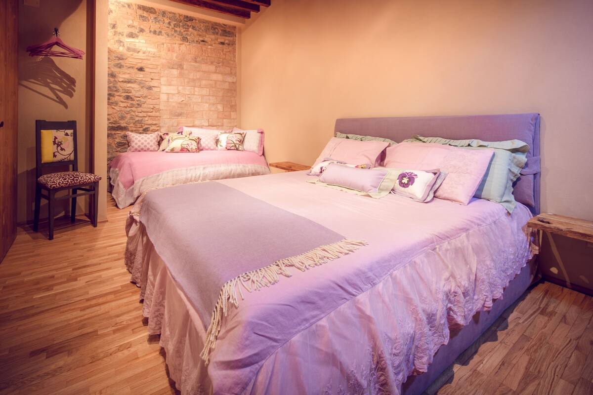 A bedroom with two beds, a wooden floor, a brick wall, and a wooden nightstand.