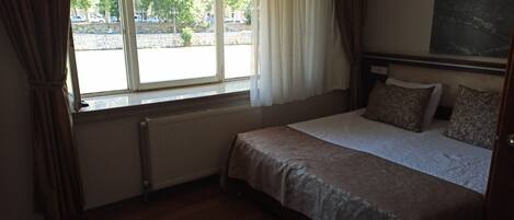 A bedroom with a bed, a radiator, a window with curtains, and a view of the street outside.