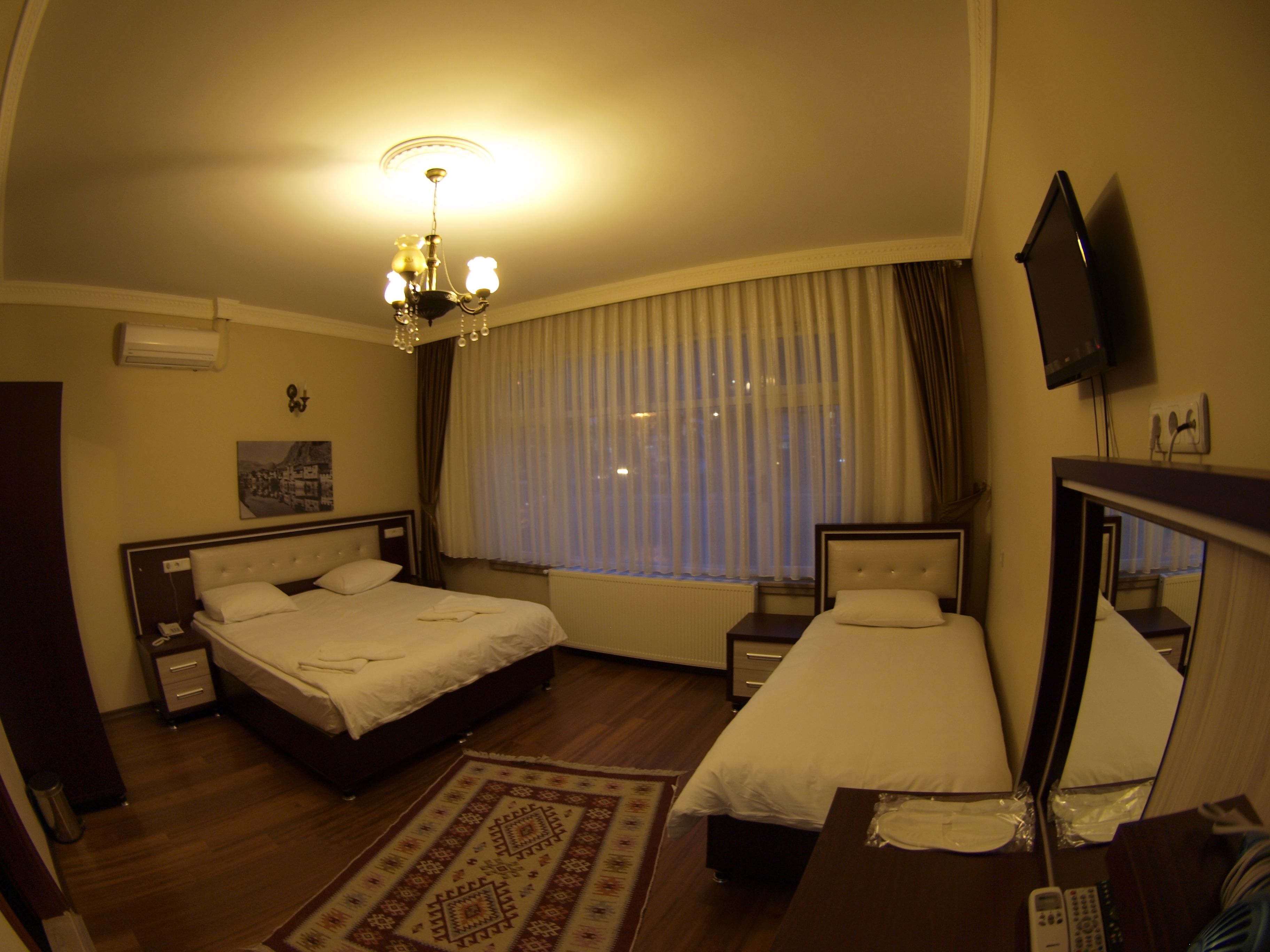 A hotel room with two beds, a chandelier, a television, and a window with curtains.