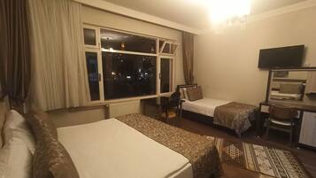 Habitación de hotel con dos camas individuales, un escritorio con silla, televisión y un ventanal con cortinas.
