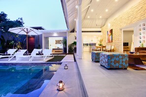 Ein moderner Poolbereich im Freien mit Liegestühlen, einem Esstisch und einer sichtbaren Küche im Hintergrund.