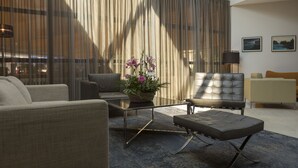 A modern living room with a sofa, armchair, ottoman, and a glass coffee table with a flower arrangement. - Zepter Hotel Drina Bajina Bašta, member of Zepter Hotels (Bajina Bašta)