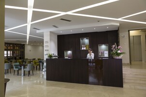 Un área de recepción con un mostrador oscuro, una recepcionista y un cartel que indica 'Reception' e 'Information Desk'.